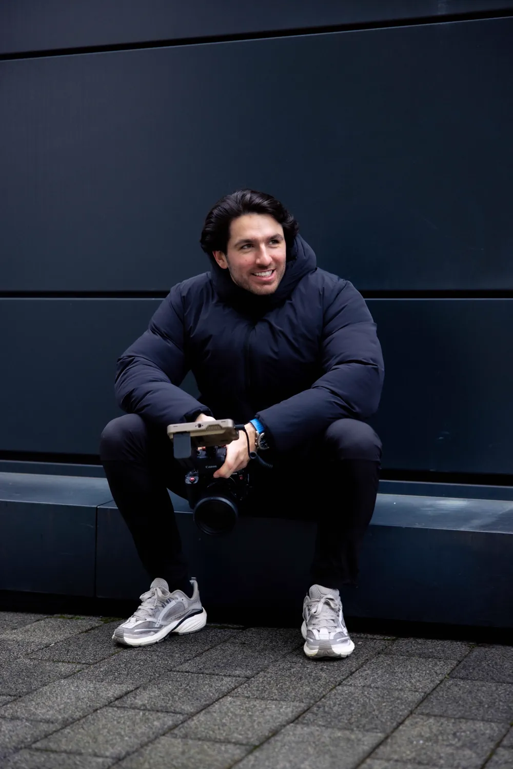Olly, sitting against a dark wall with his cinema camera.